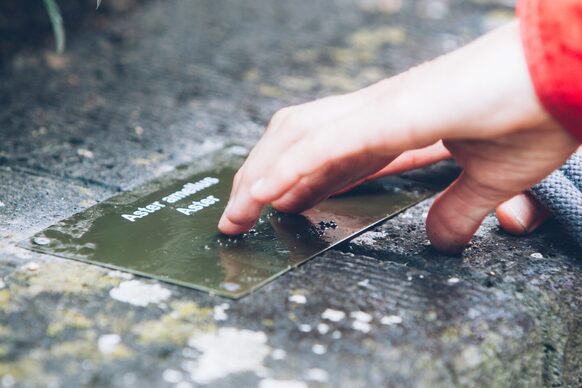 Eine Hand tastet über eine eingelassene Tafel mit Brailleschrift