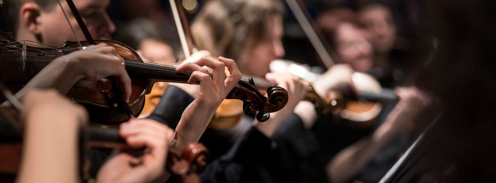 Eine Gruppe von Geiger*innen spielen Musik in einem schummrigen Raum.