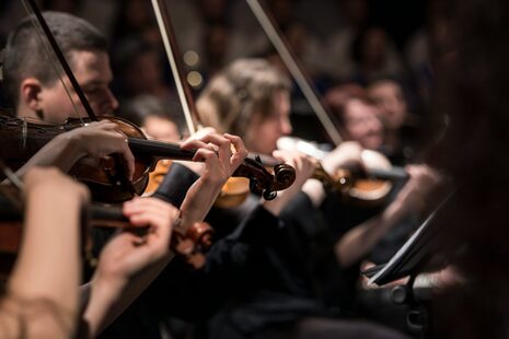 Eine Gruppe von Geiger*innen spielen Musik in einem schummrigen Raum.