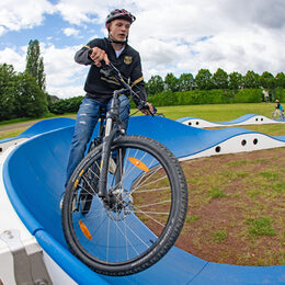 Ein junger Mann mit seinem Mountainbike auf einer blauen Fahrspur des Pumptracks