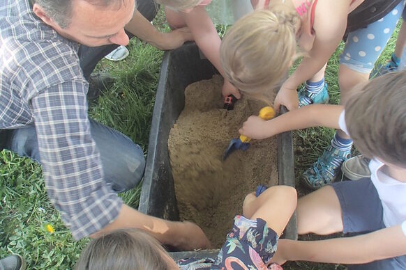 Kinder beugen sich über eine Kiste mit Sand und schaufeln darin