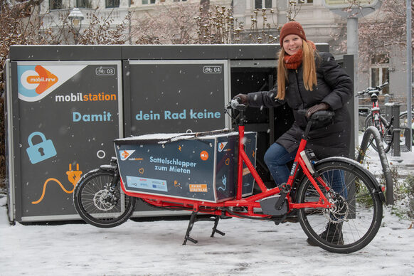 Eine Frau steht vor einer Fahrradabstell-Box mit einem Lastenfahrrad.