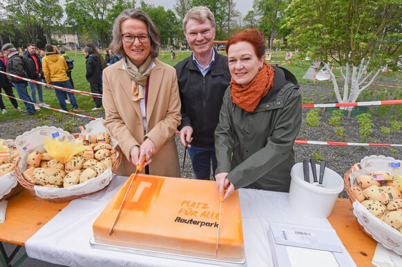 OB Katja Dörner schneidet mit Ina Scharrenbach, Ministerin für Heimat, Kommunales, Bau und Digitalisierung des Landes Nordrhein-Westfalen und Bäcker Armin Klein die Geburtstagstorte an.