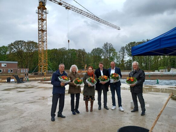 Das Foto zeigt sechs Personen mit Blumen in der Hand auf der Bodenplatte des Neubaus von Haus Elisabeth.