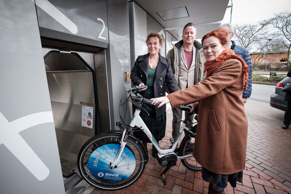 Das Bild zeigt die Bonner Oberbürgermeisterin Katja Dörner, die ein Fahrrad in eine Kabine des neuen Fahrradparkhauses in Bonn-Beuel schiebt.