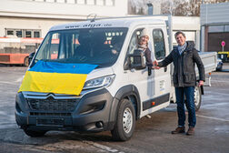 Das Bild zeigt den Pritschenwagen, der bald nach Cherson transportiert wird. Stefan Wagner vom Amt für Internationales der Stadt Bonn, übergibt den Schlüssel an Tamara Vukovic, Leiterin der Bonner Filiale Blau-Gelbes Kreuz.