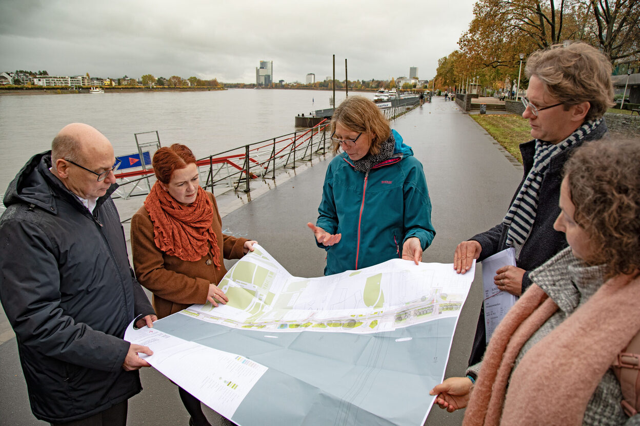 Von links: Stadtbaurat Helmut Wiesner, Oberbürgermeisterin Katja Dörner, Sandra Paul (Abteilungsleiterin im Amt für Umwelt und Stadtgrün), David Baier (Leiter Amt für Umwelt und Stadtgrün) und Doreen Käppler-Jerbi (Planerin Amt für Umwelt und Stadtgrün) mit einem Übersichtsplan zur Umgestaltung am Rheinufer stehend.