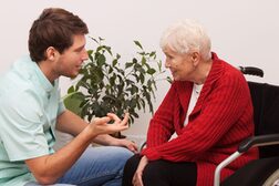 Ein Altenpfleger unterhält sich mit einer Seniorin, die im Rollstuhl sitzt