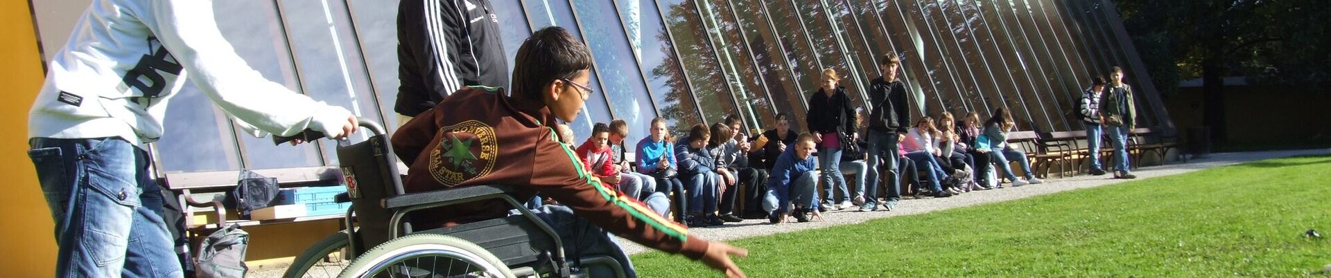 Junge im Rollstuhl spielt mit anderen Kinder Boule