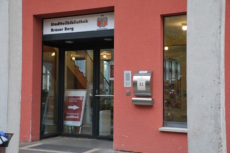 Eingang zur Stadtteilbibliothek Brüser Berg, die in einem rot angestrichenen Gebäude untergebracht ist