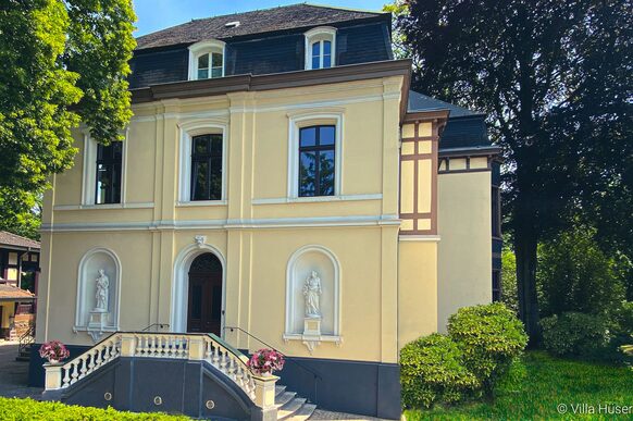 Die Villa Hüser umgeben von Bäumen und Sträuchern.