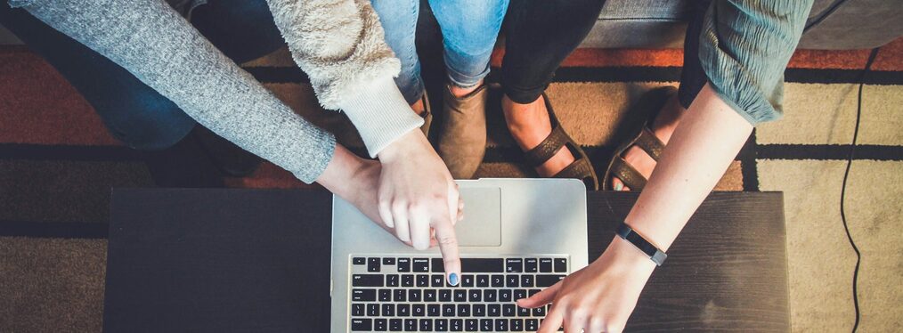 Drei Personen sitzen gemeinsam vor einem Laptop und deuten auf den Monitor