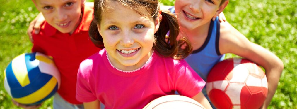 Drei Kinder auf einer Wiese mit einem Ball in der Hand.