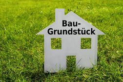 Ein Haus aus Pappe steht auf einer Wiese. Auf dem Haus steht "Baugrundstück".