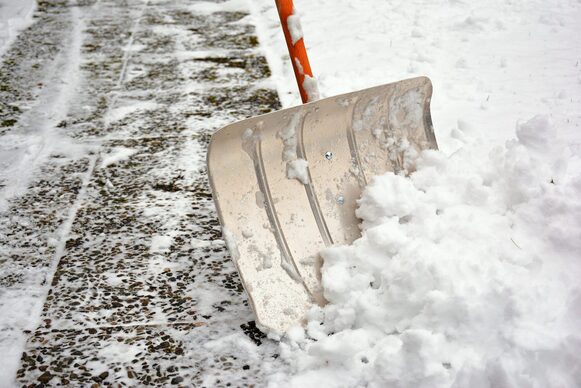 Mit einer Schneeschaufel wird Schnee von einem Gehweg geschoben