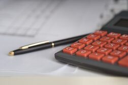 Taschenrechner mit roter Tastatur, Papier und ein Stift