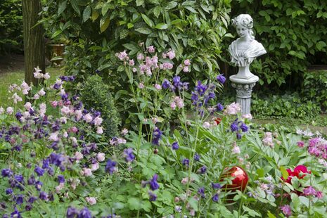 Gartenlandschaft mit blühenden Pflanzen und einer Büste