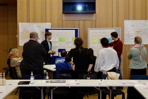 Zehn Personen stehen vor mehreren Flipcharts und unterhalten sich dabei.