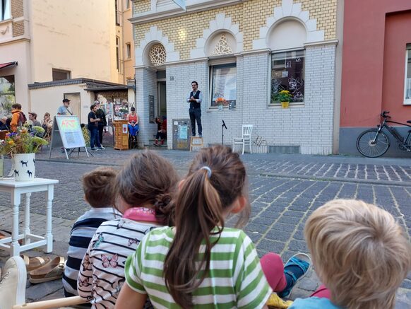 Von hinten aufgenommene Kinder schauen einem Straßenkünstler zu