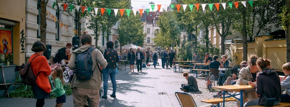 Menschen sitzen auf Bänken an einer verkehrsfreien Straße