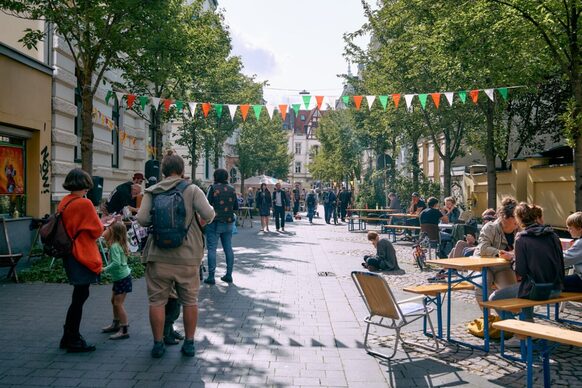 Menschen sitzen auf Bänken an einer verkehrsfreien Straße