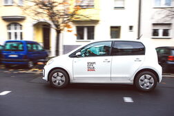 Ein weißes, kleines Elektro-Auto der Stadtverwaltung fährt durch eine Straße.