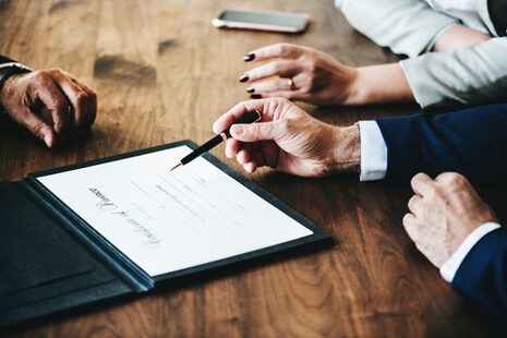 Gespräch am Tisch bei dem anhand eines Tablets Informationen erläutert werden.