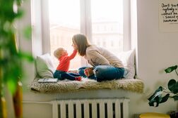 Eine Mutter sitzt mit ihrem Kind auf der Fensterbank und spielt.